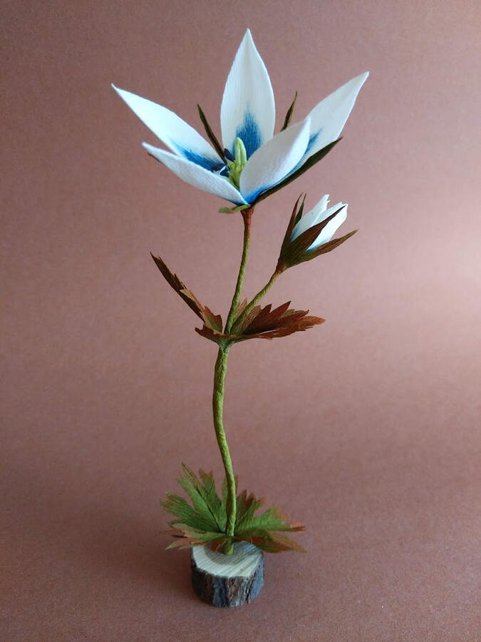 A white and blue crepe paper flower in a wood stand.