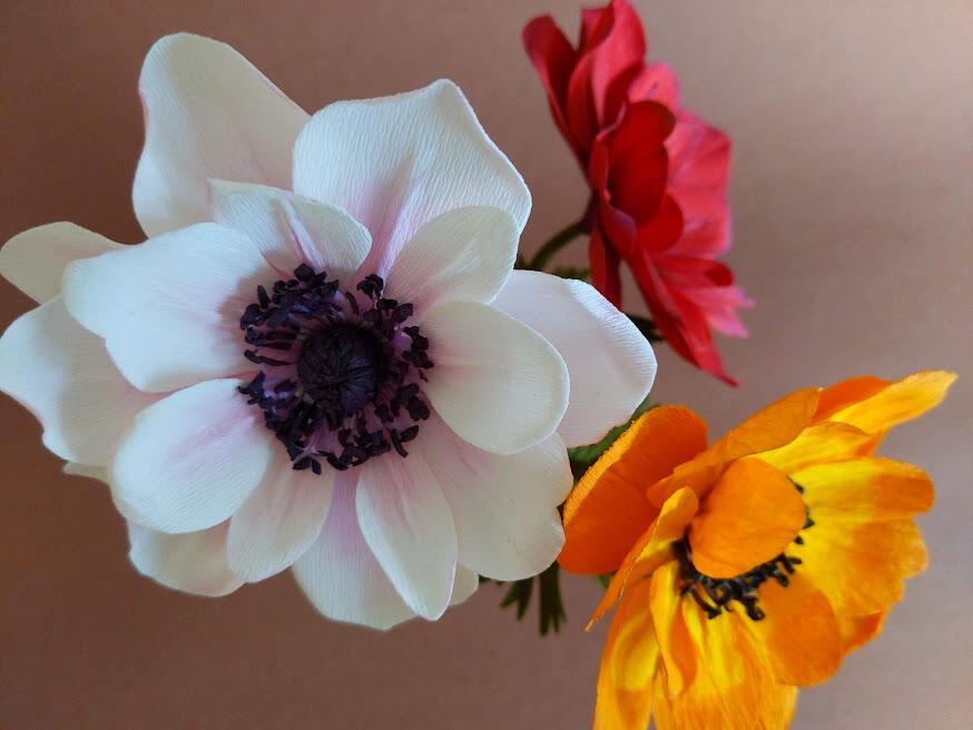 Three crepe paper anemone flowers in white, orange, and red.